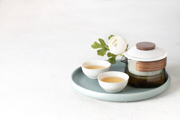 Japanese tea set , modern crystal pot and ceramic bowl cup with green tea on a try with white flowers, copy space - 776895189