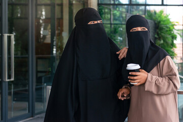 Muslim woman wearing Nigab and headscarf walks with friends in the city, one of them held a coffee...