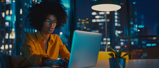 A woman with glasses concentrating on her laptop screen in an office setting.