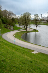 Fototapeta na wymiar Park landscape: curved footpath and cycle path, trees, green meadows and a lake in Munich, Germany