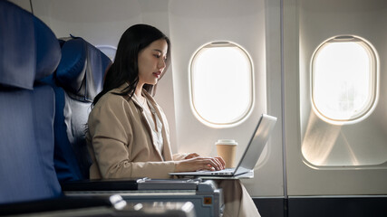 A hard-working Asian businesswoman is focusing on working on her laptop computer during the flight.