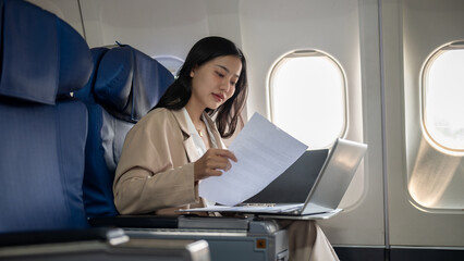 An attractive Asian businesswoman is preparing her report during the flight for her business trip.