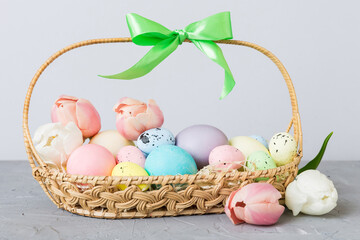 Happy Easter composition. Easter eggs in basket on colored table with yellow Tulips. Natural dyed colorful eggs background with copy space
