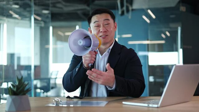 Smiling president candidate sitting at desk with laptop and talking about future innovations. Adult Chinese man dressed in blazer using loudspeaker to amplify voice while speaking with audience.
