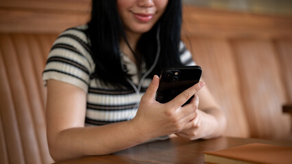 A woman sitting in a coffee shop, using her phone and listening to music on her headphones.
