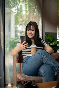 A woman relaxing in a cafe, using her smartphone and enjoying her coffee at a table by the window.