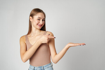 Young Woman in Tank Top Pointing at Something on gray background