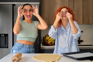 Mother and daughter making funny faces with shaped cookies molds while preparing butter cookies....