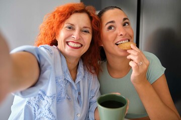 Mother and daughter taking a selfie while eating homemade butter cookies and coffee. Family time.