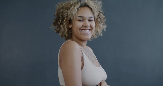 Slow motion portrait of good-looking African American lady in underwear stroking body and smiling standing on gray background. Attractive woman and positive emotion concept.