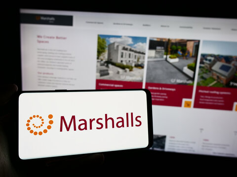 Stuttgart, Germany - 03-25-2024: Person holding cellphone with logo of British landscaping products company Marshalls plc in front of business webpage. Focus on phone display.