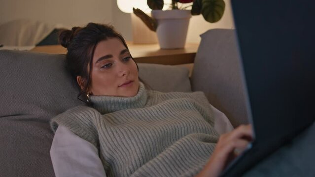 Calm girl relaxing sofa typing laptop at night home closeup. Woman resting couch