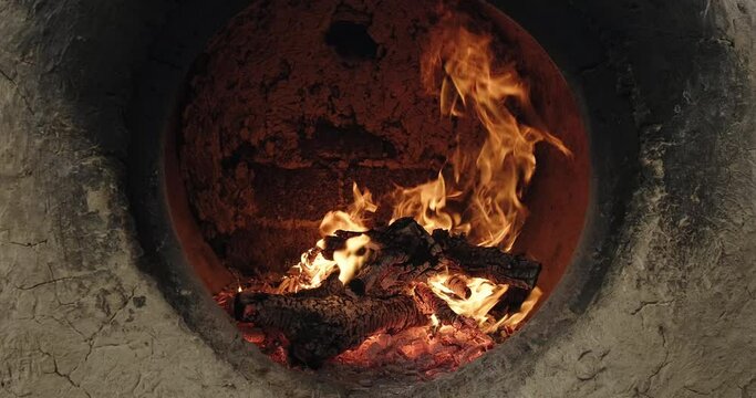 Firewood burns brightly in a clay Uzbek oven tandoor to bake samsa or bread. Burning fire in stone oven. Uzbek bakery