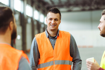 Attractive, smiling man, foreman wearing workwear, talking with colleagues, standing in warehouse