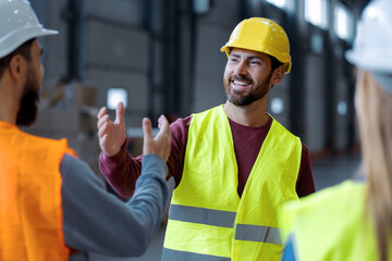 Handsome, smiling, bearded, middle aged man wearing protective helmet shaking hands with colleagues