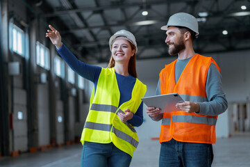 Attractive smiling woman working with her foreman, pointing hand while standing in warehouse