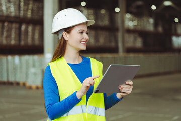 Smiling female architect wearing white hard hat and workwear holding digital tablet using mobile app
