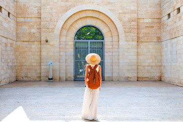 Back view of a hipster girl traveler in a hat and backpack traveling alone through the sights of Israel. - 776958978