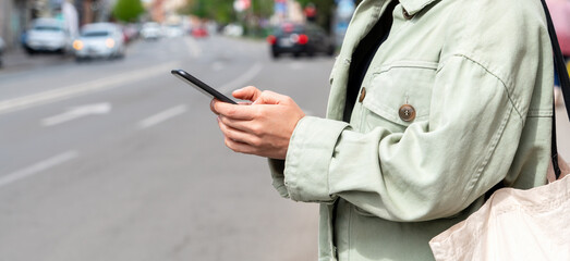 Female person uses mobile phone to search for car rental, car-sharing or taxi while standing by the roadside in city.