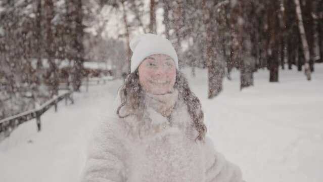 Portrait of a smiling happy woman throwing snow up. Beautiful playful girl enjoying a walk outdoors, having fun during winter holidays. Happy pleasure concept