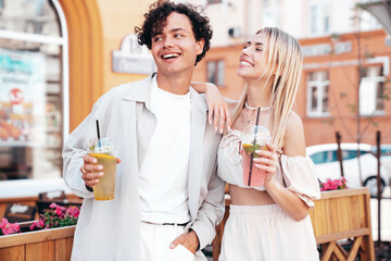 Young smiling beautiful woman and her handsome boyfriend in casual summer clothes. Happy cheerful family. Female having fun. Couple posing in street. Holding and drinking cocktail drink in plastic cup