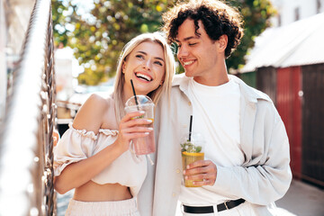 Young smiling beautiful woman and her handsome boyfriend in casual summer clothes. Happy cheerful family. Female having fun. Couple posing in street. Holding and drinking cocktail drink in plastic cup
