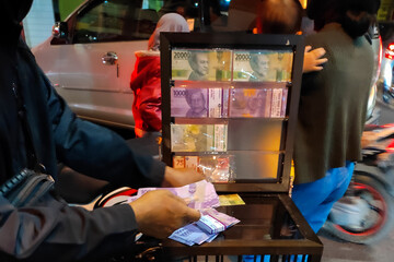 
A small money exchange service is serving customers converting money into Rp.10,000 bills. This business thrives before Eid across Indonesian cities.