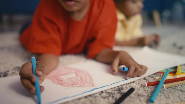 Little African American boy drawing while lying on floor, creativity and hobby
