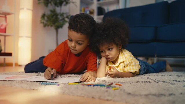 Cute African American boys drawing with pencils, playing on the floor at home