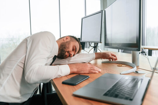 Tired, sleeping on the table. Businessman is sitting by computer and working in the office