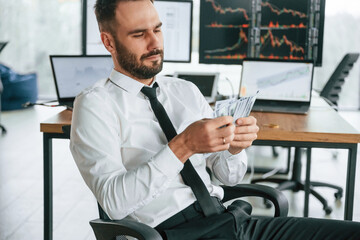 Counts money. Businessman is sitting by computer and working in the office