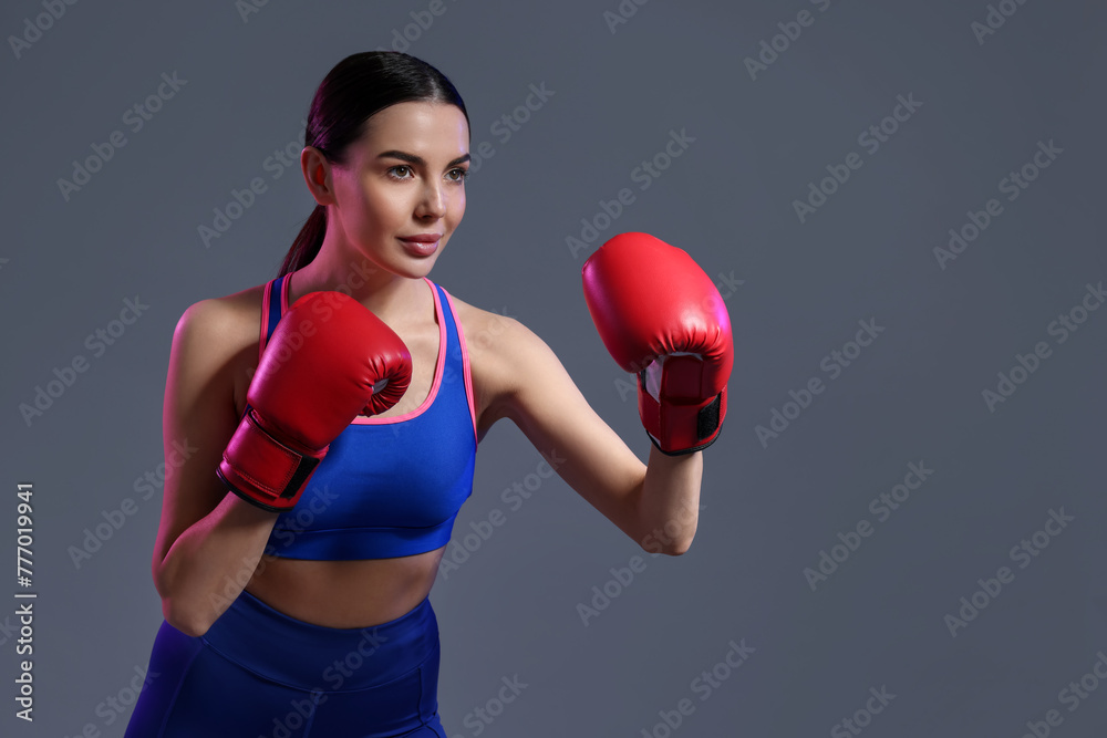 Canvas Prints Beautiful woman wearing boxing gloves training in color lights on grey background. Space for text