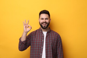 Happy young man with mustache showing OK gesture on yellow background