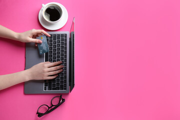 Online payment. Woman with laptop, credit card, glasses and coffee on pink background, top view....