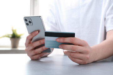 Online payment. Woman with smartphone and credit card at white table, closeup