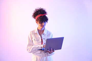 Beautiful young woman with laptop on color background in neon lights
