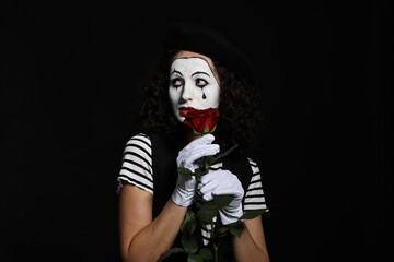 Young woman in mime costume with red rose posing on black background