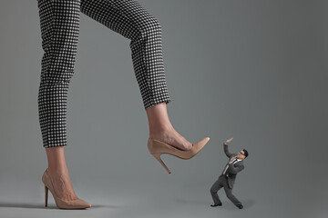Big woman stepping onto small man on grey background - obrazy, fototapety, plakaty
