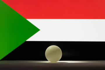 The table tennis ball stands on a surface in front of Sudan flag.