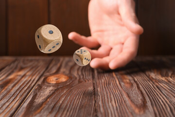 Man throwing dice on wooden table, closeup