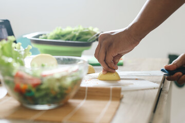 Male hand cutting lemon with knife on chopping board in the kitchen, prepare making salad