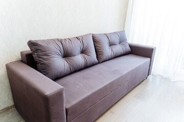 Furniture A brown couch in a living room by window, on hardwood flooring