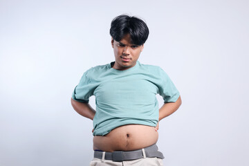 Funny young Asian man with a big belly standing and looking at camera confidently. Diet and healthy...