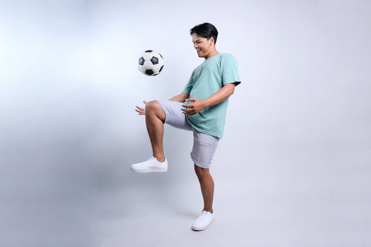 Full length view of young Asian stylish man playing soccer with happy expression