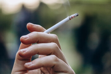 A man's hand holds a thin smoking cigarette