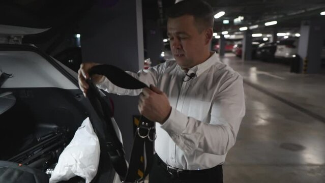 Male photographer in white shirt putting on leather camera straps in parking lot. Accessories for professional photography.