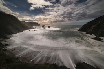 moments before dawn, in the blue hour on the beach of silence in Asturias with clouds in the sky