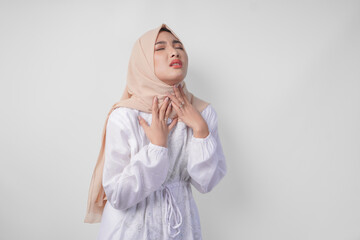 Tired Asian Muslim woman in white dress and hijab holding her neck feeling thirsty waiting for...