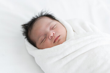 Adorable newborn baby wrapped in white swaddle towel lying on bed and sleeping peacefully. Sleeping...