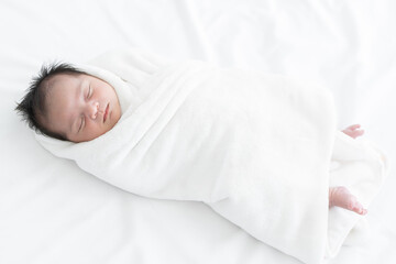 Adorable newborn baby wrapped in white swaddle towel lying on bed and sleeping peacefully. Cute...